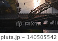 Aerial telephoto tracking shot of a lone pedestrian crossing the Wearmouth Bridge at sunrise in Sunderland, with the industrial architecture of the Monkwearmouth Railway Bridge in the foreground. 140505542