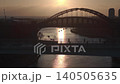 Aerial drone shot flying backwards and ascending from the silhouetted Keel Crossing, revealing the Wearmouth Bridge and Monkwearmouth Railway Bridge against a golden sunrise in Sunderland. 140505635