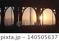 Fast aerial tracking shot of the Wearmouth and Monkwearmouth Railway Bridges in silhouette against a golden sunrise in Sunderland, featuring commuters and city traffic. 140505637