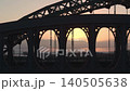 Aerial silhouetted shot of the Monkwearmouth Railway Bridge and Wearmouth Bridge at sunrise, featuring a Tyne and Wear Metro train crossing as the sun peeks through the industrial ironwork. 140505638