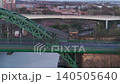 Aerial telephoto tracking shot moving laterally past the Wearmouth Bridge in Sunderland at dawn, showcasing early morning traffic commuting over the River Wear with industrial architecture in the back 140505640