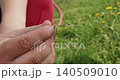 Close-up view of a man's hand gently holding a small green lizard with black spots. The wild reptile, caught in the garden, opens its mouth and looks around while being held outdoors. 140509010
