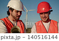 Senior engineers at wind farm confirm successful commissioning wind turbines. White helmet engineer and red helmet engineer hold project papers shake hands and show satisfaction after completion clean 140516144