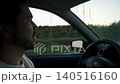 Driver operates windshield wipers to clean dirty windshield during long rural drive. Water and wiper movement remove dust and streaks while forest road continues outside vehicle under fading daylight 140516160