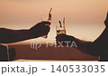 A couple of lovers drinking a mojito cocktail on the beach, cocktail glasses and hands in close-up, a view of the garden against the background of an orange sunset. they clink glasses and say Cheers 140533035