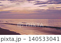 The sun sets on the beach as the sky changes color. Waves roll onto the shore, creating a rhythmic sound. The water reflects the soft light as evening arrives. High quality 4k footage 140533041