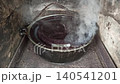 Traditional Cooking Pot with Steam in Old Stone Oven. Hot food or jam boiling in large cauldron over open fire. Boiling cauldron in stone oven. Jets of steam escape from under the lid on pot of soup 140541201