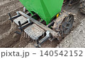 green potato planter machine attached to tractor working in agricultural field. Planting potatoes process in open soil. Farming equipment and rural seasonal industrial work. 140542152
