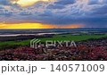 Aerial panoramic view of a Dutch town with red roofs, green fields, and a distant city skyline under a dramatic sunset sky with storm clouds in the Netherlands. 140571009