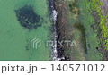 Top down aerial view of turquoise ocean water, rocky breakwater shoreline with sea foam, and green mossy coast in the Netherlands during spring. 140571012