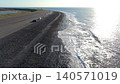 Aerial view of the Westkapelle sea dike with a rocky breakwater coast, parked camper vans, a distant lighthouse, and bright sun glare on the North Sea in Zeeland, Netherlands. 140571019