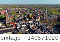 Aerial panoramic view of a traditional Dutch town with historic brick churches, red rooftops, and lush green trees under a clear blue sky in Gelderland, Netherlands during spring. 140571020