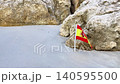 Spanish flag positioned among rocks on sandy beach, showcasing vibrant colors of red and yellow, with natural textures of stone and sand creating a serene coastal atmosphere 140595500