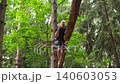 A man goes through a difficult obstacle course on suspended logs at a height. A man with safety equipment in an active recreation park. 140603053