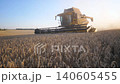 Modern harvester gathering crop of ripe wheat in field at sunset time. Combine riding through rural cutting yellow stalks of barley. Scenic view of grain field at background. Working process on farm 140605455