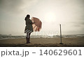 Caucasian woman opens beach umbrella on seashore. Person sets up aesthetic sun umbrella at dawn on wide shot. 140629601