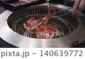 Delicious slices of marinated meat grilling on metal mesh over hot coals in a traditional BBQ restaurant. Authentic Japanese yakiniku or Korean barbecue cooking process with metal tongs. 140639772