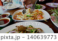 Thai spicy green papaya salad or Som Tum served on a white plate in a restaurant. Accompanied by various side dishes like spicy minced meat and fresh vegetables for an authentic dining experience. 140639773