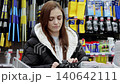 Young woman examines a pair of winter boots in a sporting goods store, carefully weighing her options before making a purchase decision 140642111
