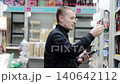 Man in casual attire examines hygiene products on a supermarket shelf while holding a smartphone. Engaging in decision making, he assesses options and reviews product details 140642112