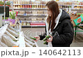 Young woman examining avocados on a supermarket shelf. Holding two ripe avocados, she assesses their quality and chooses the best one for purchase 140642113