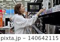 Young woman shopping for a microwave oven, opening and closing various models while comparing features and prices 140642115