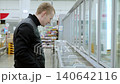 Customer selecting a frozen food item in a supermarket, weighing various options in the freezer aisle while considering choices for a nutritious diet 140642116