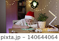 Child with cast on hand writing letter to Santa at writing desk in decorated room. Expectation of Christmas miracle, fulfillment of cherished wishes, naive child belief in magic. 140644064