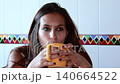 Beautiful thoughtful woman drinking a hot beverage from a yellow mug in a kitchen, looking into the camera. Slow motion clip about lifestyle, relaxation and enjoying a quiet moment at home 140664522