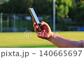 Male hand scrolling content on smartphone near football stadium field at sunset, close up of man using mobile phone browser outdoors, social media browsing, mobile internet, online communication 140665697