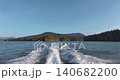 Vessel leaving wake on calm water past coastline 140682200