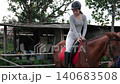 Young rider learns horseback balance during guided lesson beside rustic stable 140683508