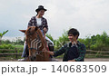 Smiling rider on brown horse guided by handler in rural paddock under soft daylight 140683509