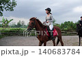 Smiling woman riding brown horse while second rider follows in outdoor arena sequence 140683784