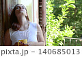 Pensive young woman looking out the window while holding a yellow mug, feeling melancholic and thoughtful in the morning sunlight as she enjoys her coffee and contemplates life 140685013
