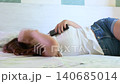 Depressed young woman feeling lonely and sad while lying in bed listening to music on her smartphone with earphones, looking at the ceiling and then closing her eyes in her bedroom 140685014