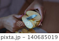 Feminine hands with red nail polish carefully cutting a fresh yellow apple into thin slices with a kitchen knife and placing them on a plate, preparing a healthy organic fruit snack 140685019