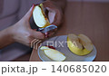 Close up view of female hands carefully cutting a fresh yellow apple into slices with a kitchen knife and arranging them on a white plate, preparing a healthy and delicious fruit snack 140685020