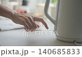 Hand places electric kettle on base and presses power switch on kitchen counter 140685833