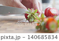 Hand cuts tops off fresh strawberries with knife on cutting board 140685834