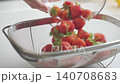 Strawberries are poured from glass bowl into metal sieve 140708683