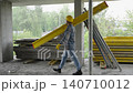 Construction worker carrying heavy beam on building site 140710012
