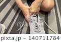 Caucasian lady secures sneaker tight, Person ensures shoelaces are tied securely before exercise start, Preparatory step where woman tightens sneaker laces for comfortable fit before activity 140711784