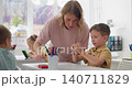 Close-up of tattooed hands holding a small colorful object in a sunlit room 140711829
