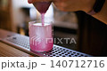Drink making. Cold cocktail. Bartender hand straining pink liquid in glass with large ice cube. Mixology process at metal pub counter. 140712716
