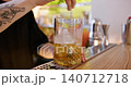 Preparing drink. Ice cocktail. Bartender hand professionally stirring yellow cold liquid with long metal spoon in glass on pub counter. 140712718
