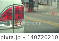 Stationary shot focusing on the rear tail light of a white vehicle. Other commuter cars are captured driving past on the busy asphalt road in soft natural daylight. 140720210