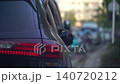 Tight shot showing the rear end of a black car parked by the roadside. The footage exhibits subtle camera movement with a blurry motorcycle rider moving in the background. 140720212