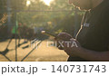 White man using smartphone near football field at sunset while players train in background. Concept of phone addiction, social isolation, procrastination, digital distraction, unhealthy lifestyle 140731743