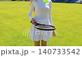 Young woman practicing tennis ball control with racket on an outdoor clay court, female athlete in white sportswear improving coordination skills during sunny day training session, handheld shot 140733542